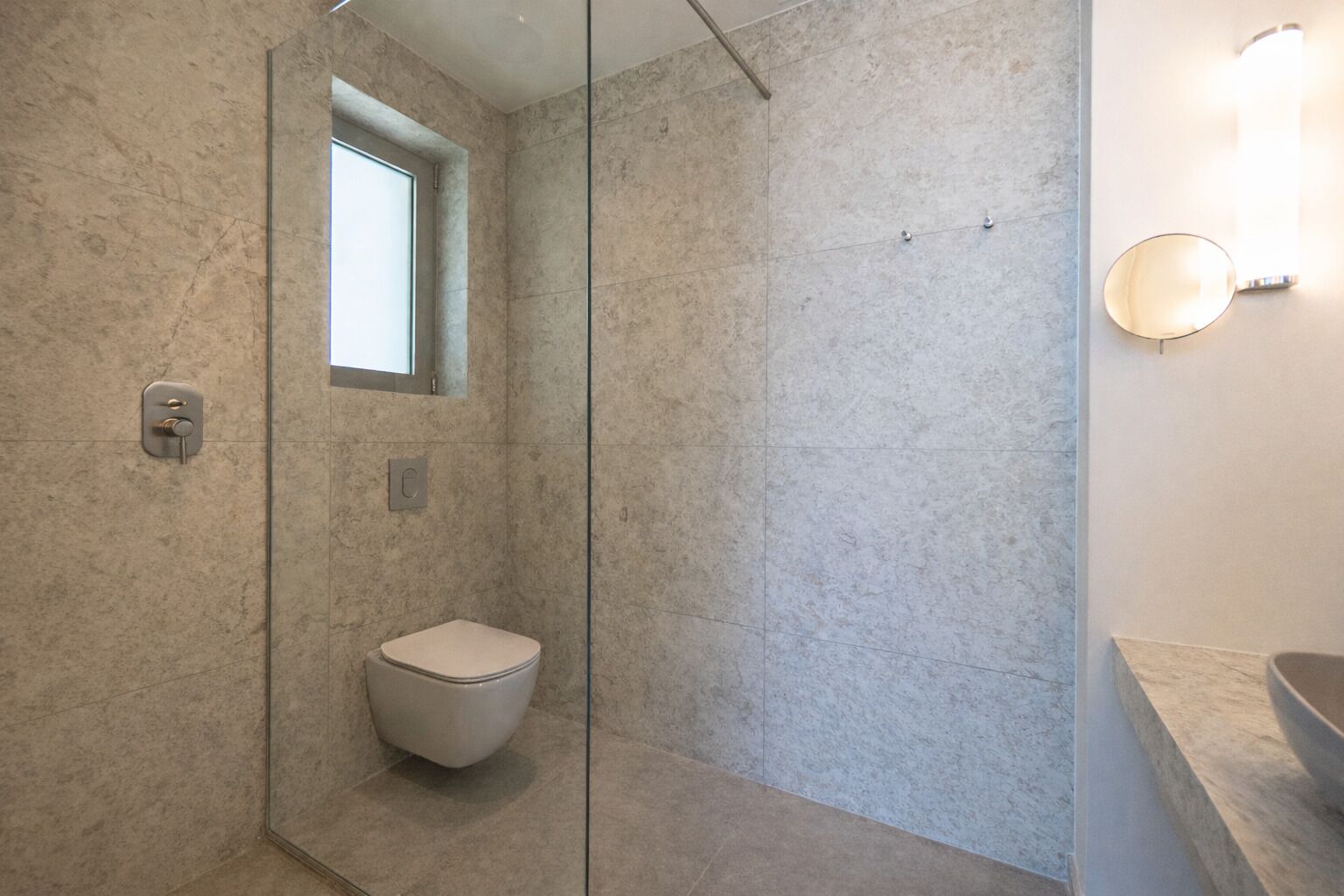 Un baño moderno con cabina de ducha de vidrio, inodoro y encimera de mármol.
