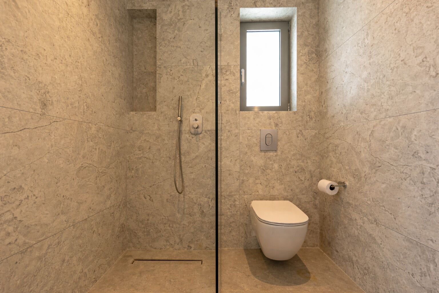 Un baño con ducha, inodoro y un pequeño ventanal.