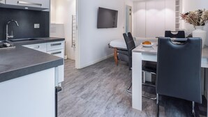 Una cocina moderna con estufa integrada, un comedor con mesa y sillas, y un armario blanco con un televisor de pantalla plana montado encima.
