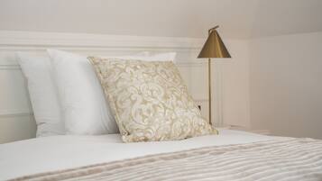 A neatly made bed with white and patterned pillows, a gold-colored lamp, and a white headboard.