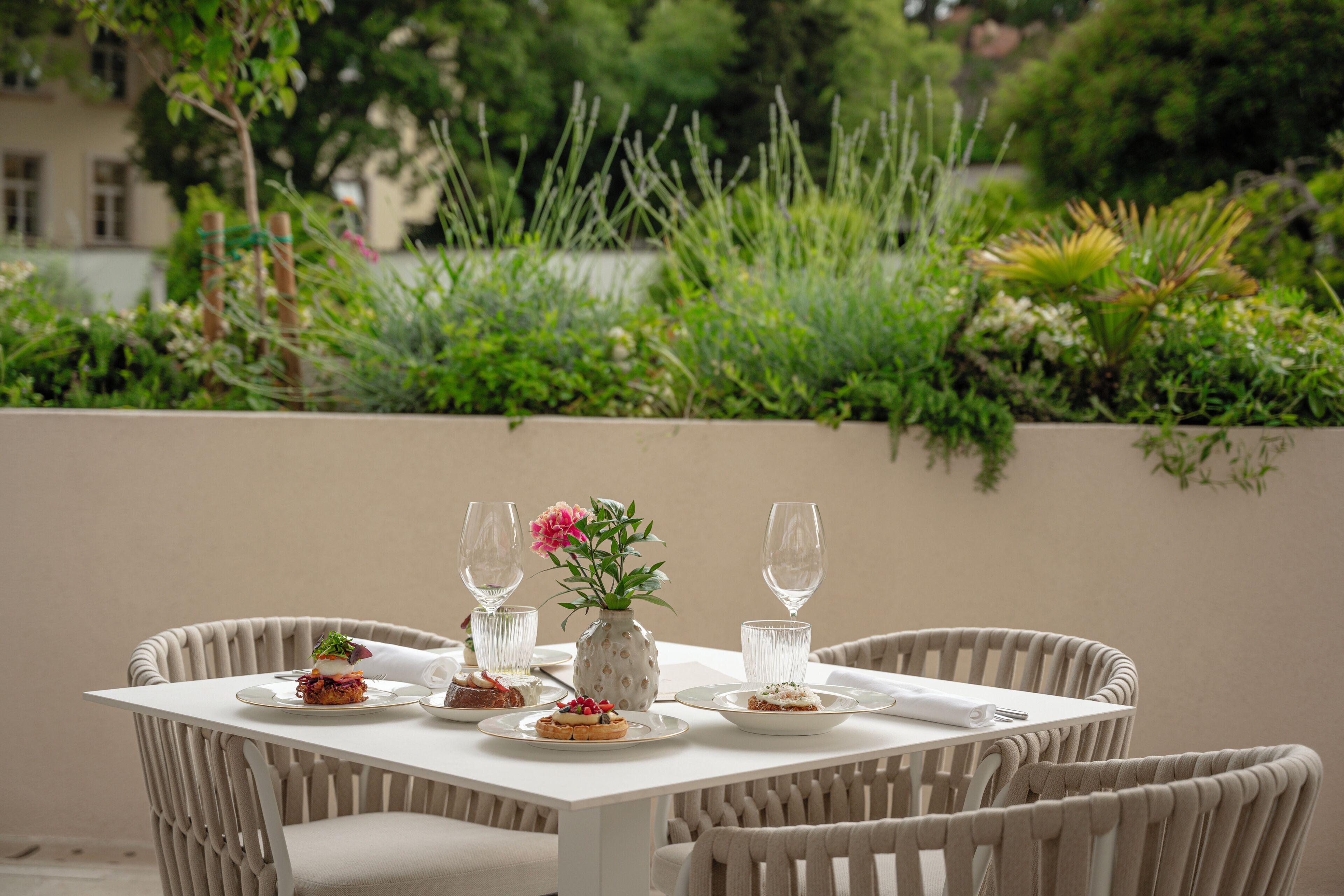 A dining table with plates of food, glasses, and a vase with flowers.