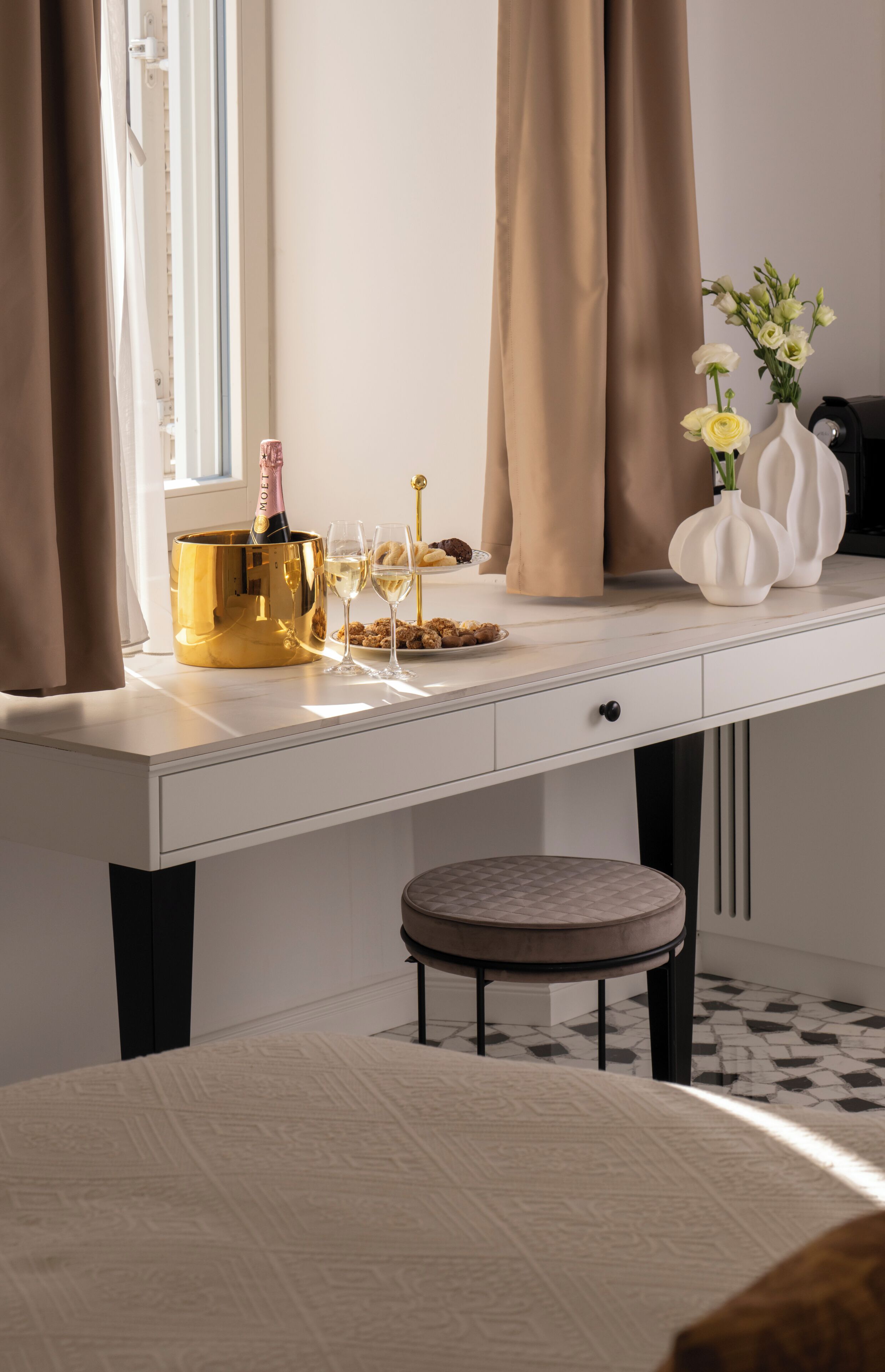 Een wit bureau met een gouden emmer, champagne, glazen en een bord gebakjes.
