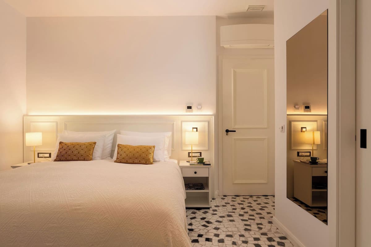 Een hotelkamer met een groot bed, nachtkastjes met lampen, een nachtkastje, een spiegel en een deur naar een andere kamer.