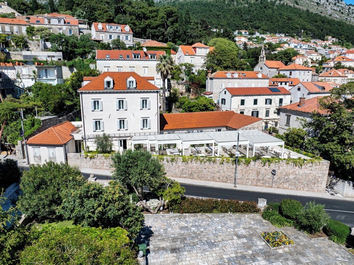 A hillside town with terracotta-roofed buildings, a prominent white building with a balcony, and lush greenery.