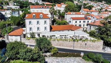 A hillside town with terracotta-roofed buildings, a prominent white building with a balcony, and lush greenery.