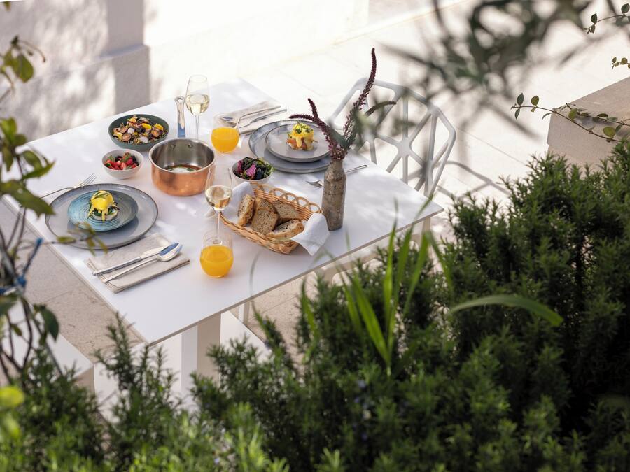 A table set for dining outdoors with various dishes, a vase, and a glass of orange juice.