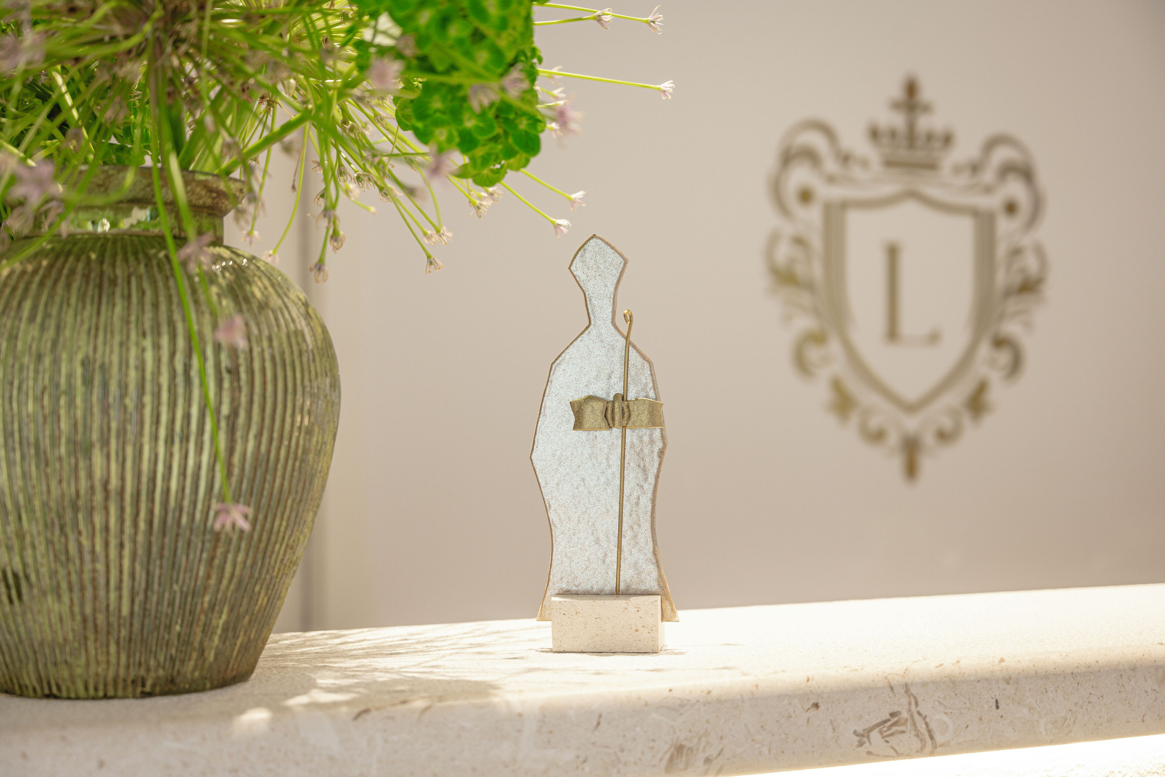 A vase with flowers, a decorative bottle, and a coat of arms on a wall.