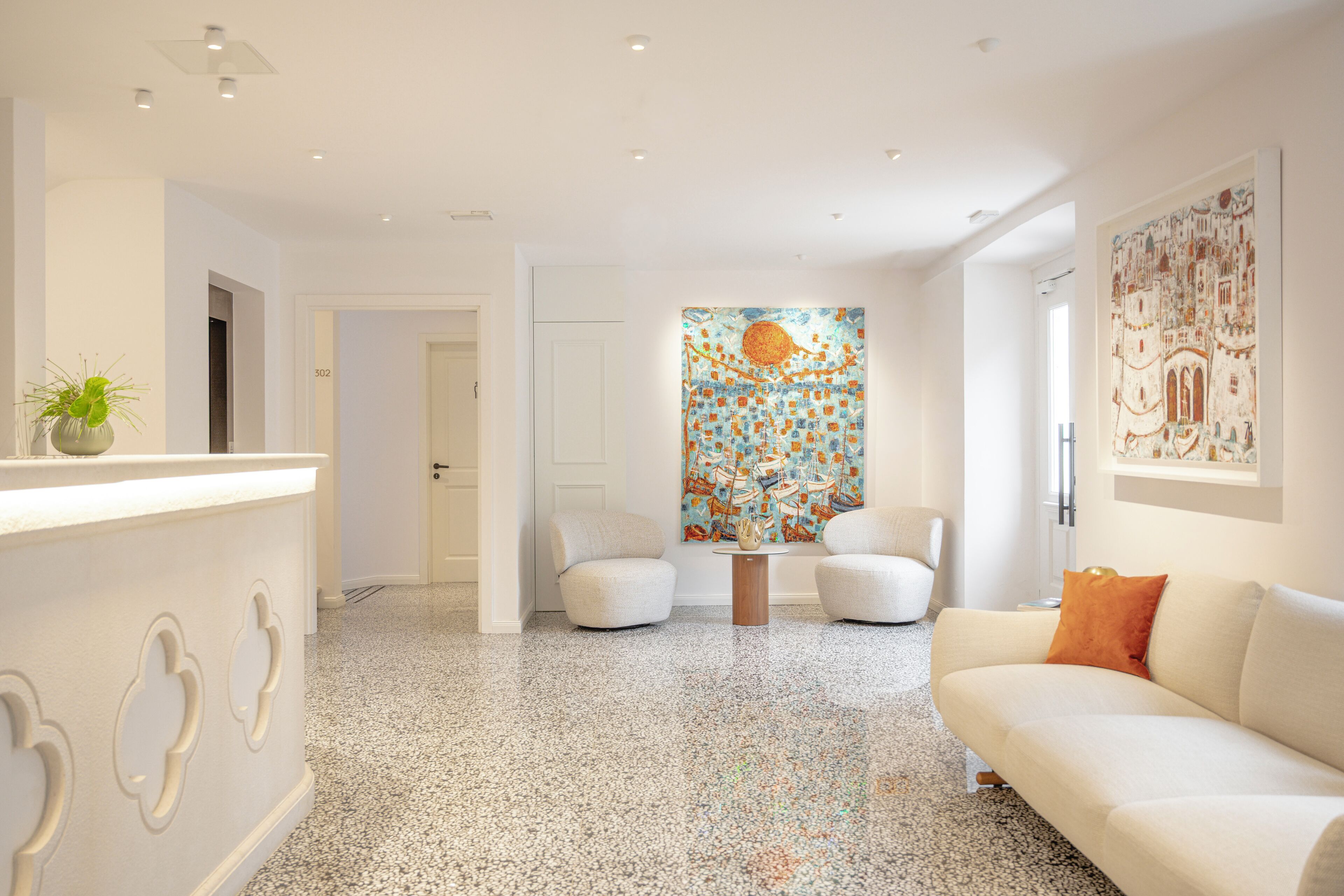Un salon moderne avec un canapé blanc, deux fauteuils, une table basse et une peinture abstraite aux couleurs vives accrochée au mur.