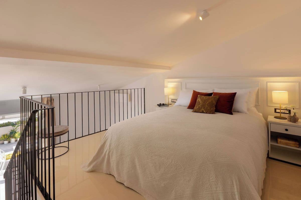 Een ruime slaapkamer met een groot bed, een balkon met hekwerk en uitzicht op de omgeving.