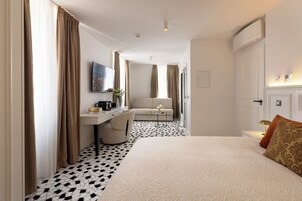 Quarto de hotel com uma cama, uma escrivaninha, uma cadeira, um sofá e uma mesinha de cabeceira com abajur.