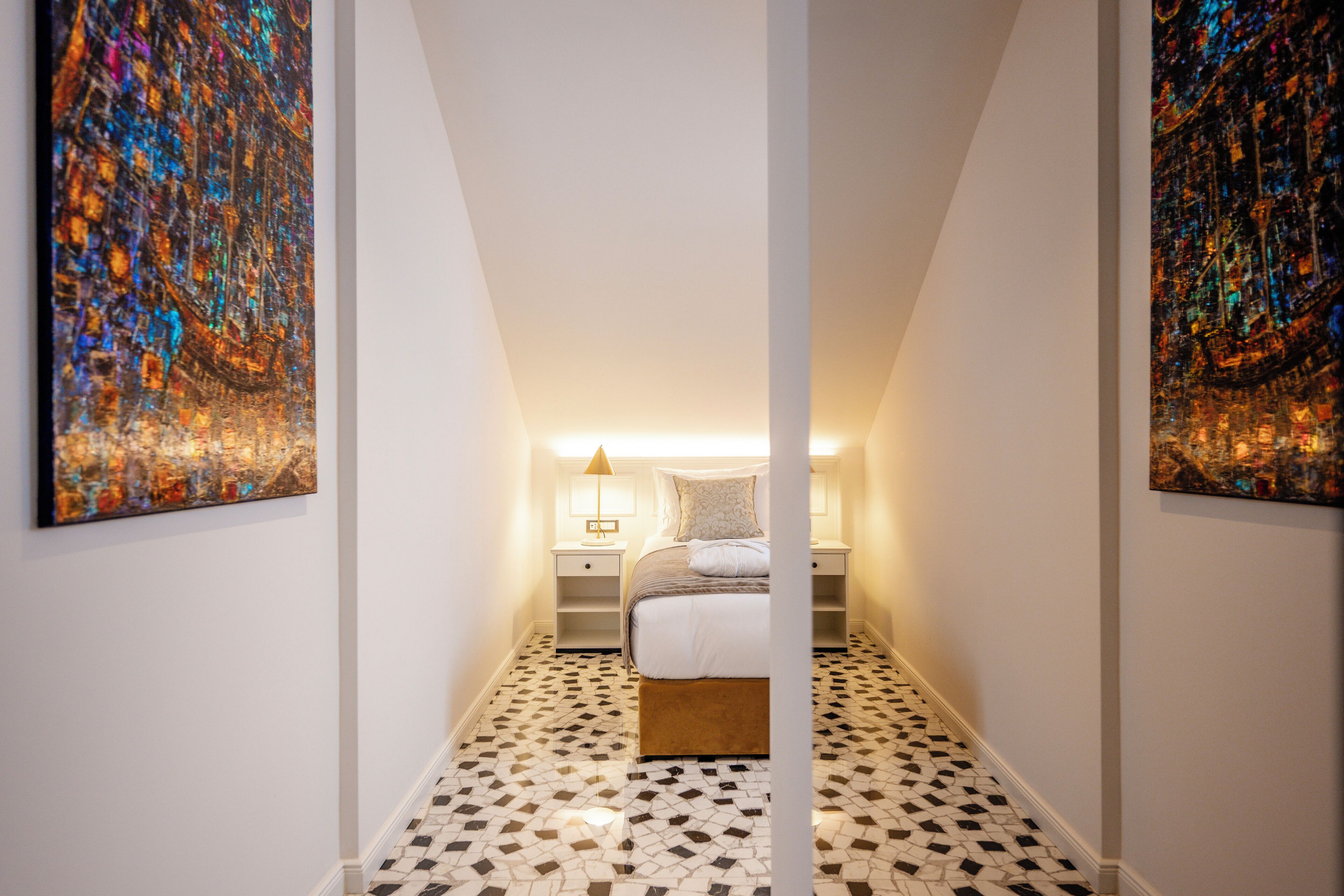 A narrow hallway leading to a bedroom with a bed, nightstands, and a patterned floor.