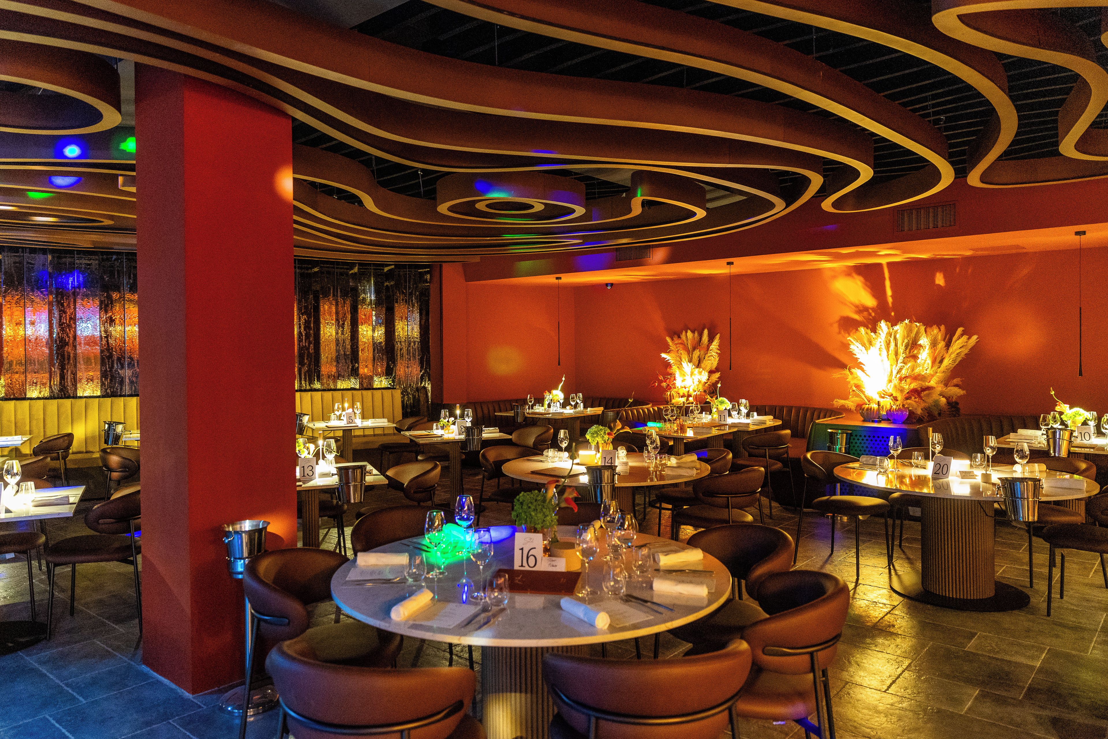 A restaurant interior with round tables, chairs, and a modern ceiling design.