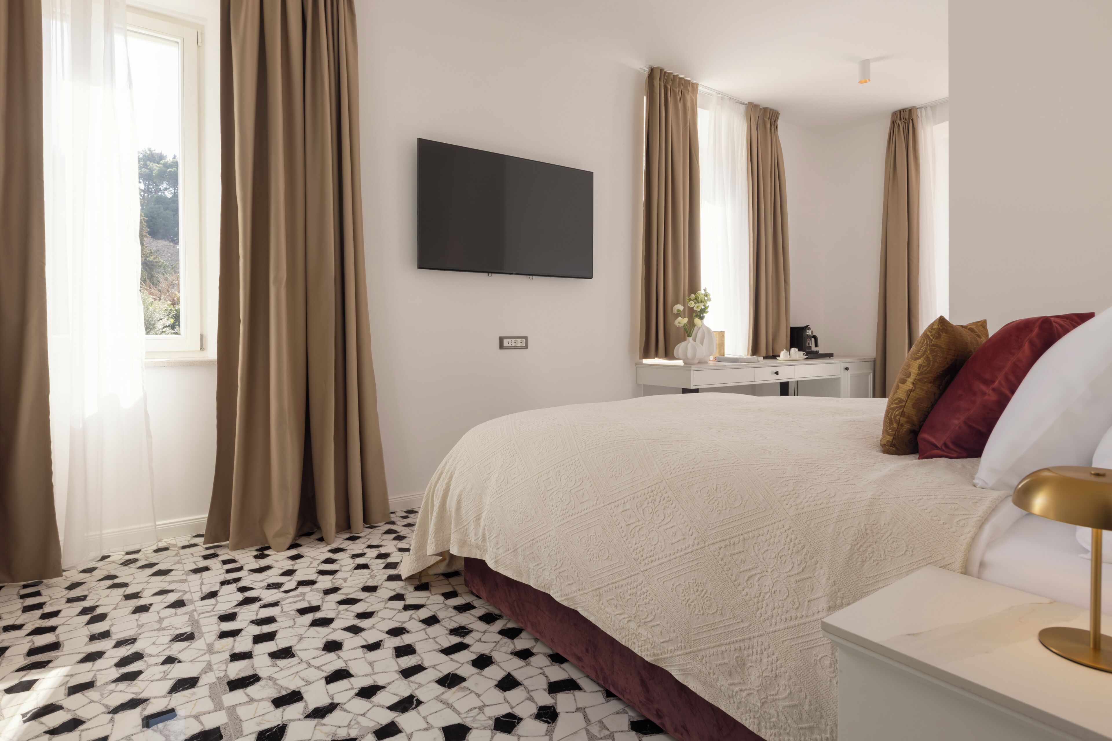 A hotel room with a bed, a flat-screen TV, a nightstand, and a window with curtains.