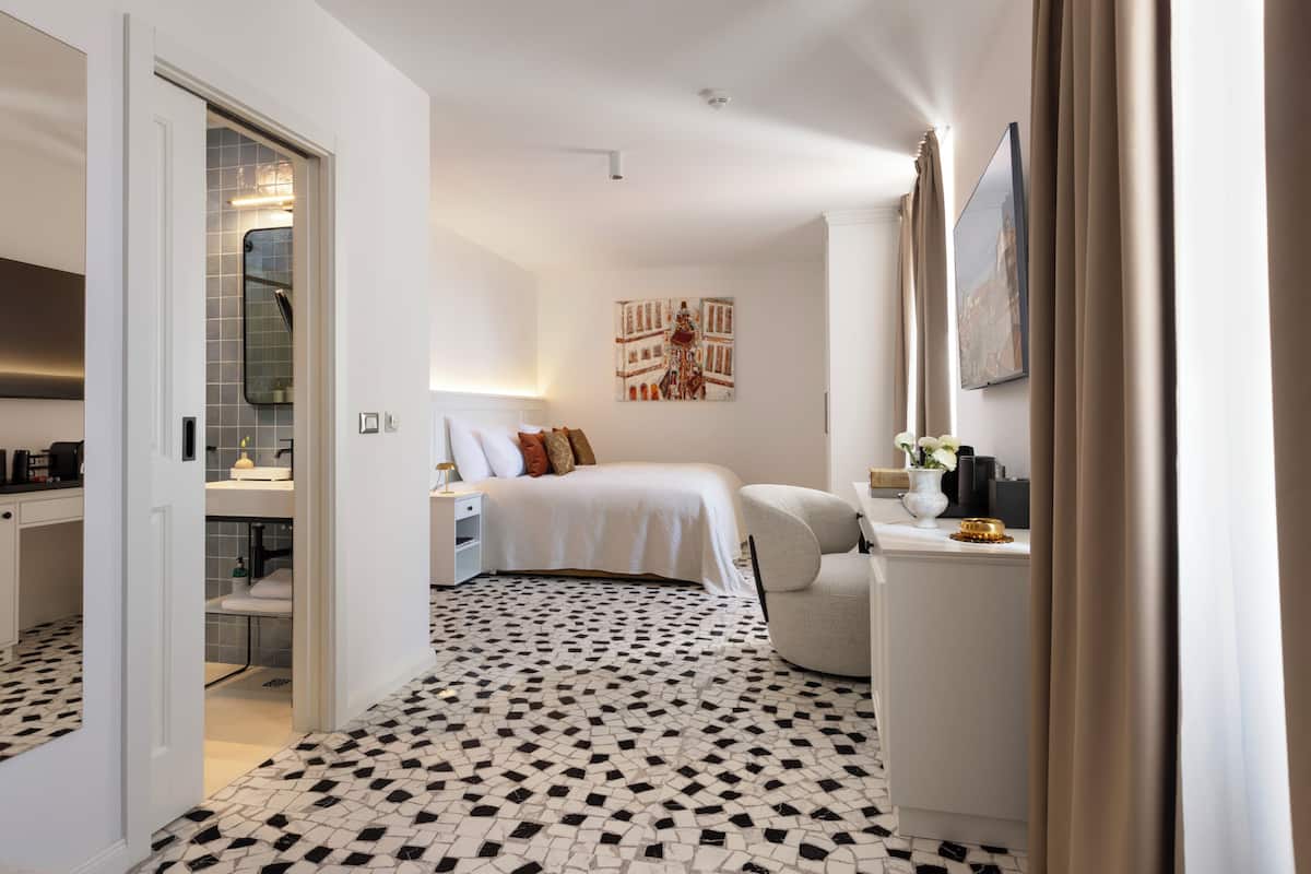 Een hotelkamer met een bed, nachtkastje, stoel en een betegelde vloer.