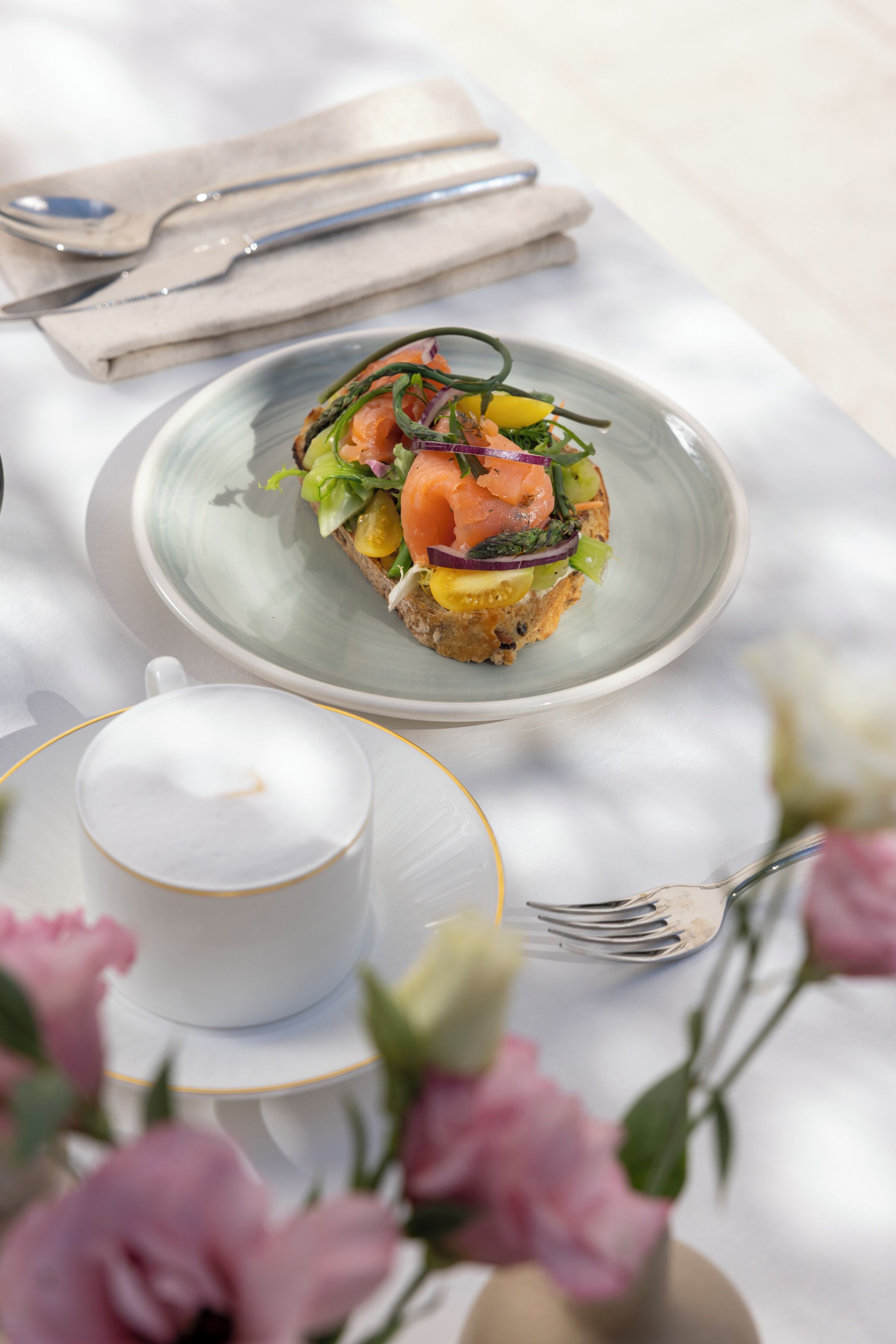 Una mesa con un plato de comida, una taza de café y un jarrón con flores.