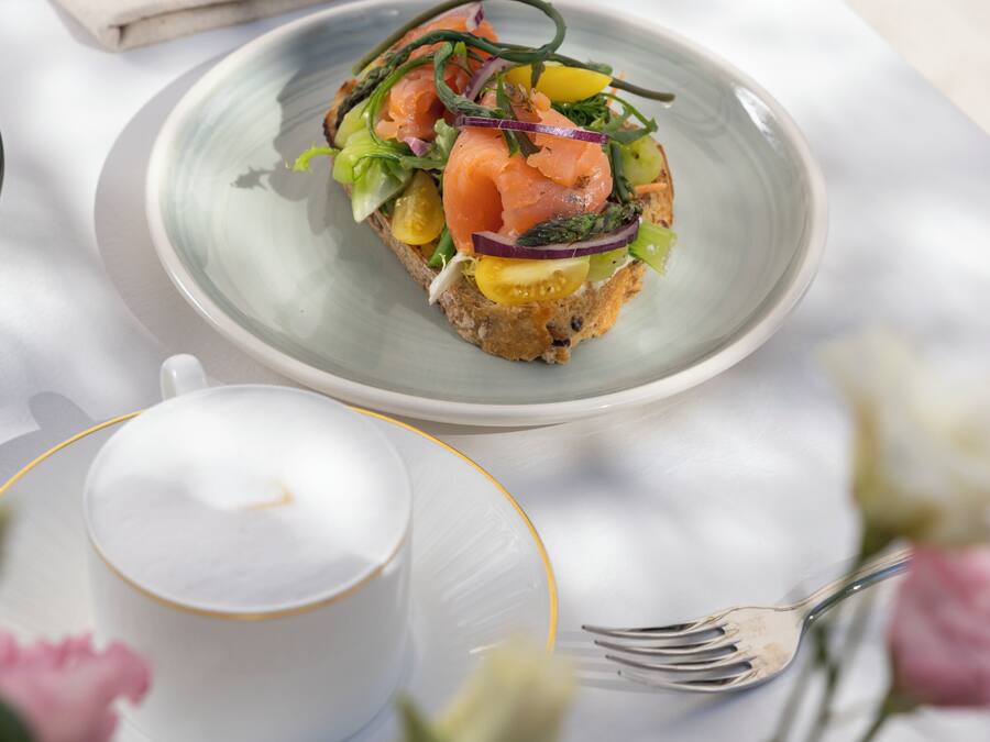 Una mesa con un plato de comida, una taza de café y un jarrón con flores.