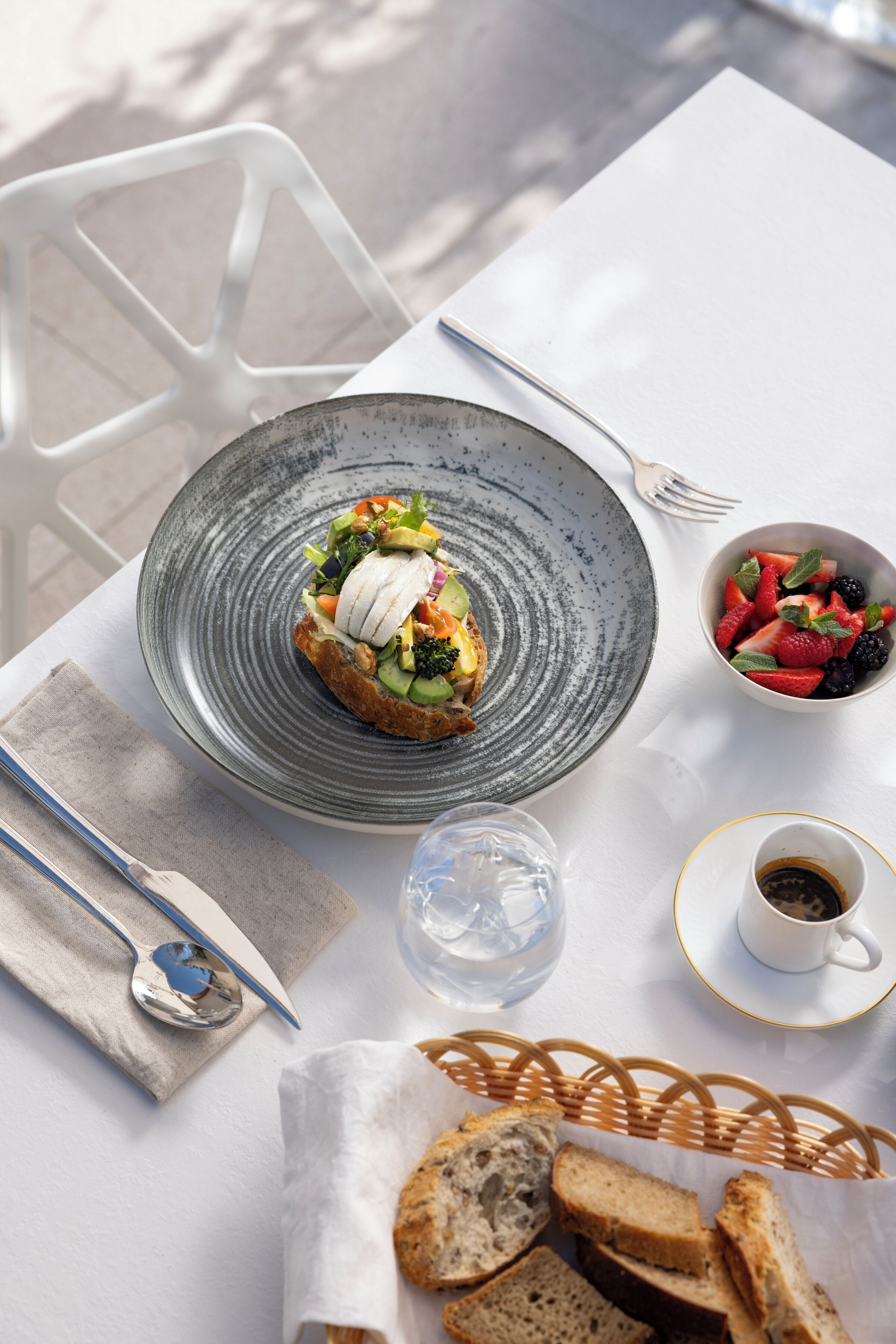 A table with a plate of food, a bowl of fruit, a cup of coffee, and a basket of bread.