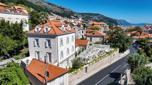Un borgo costiero con edifici a tetto di tegole rossastre, una strada ben tenuta e montagne sullo sfondo.