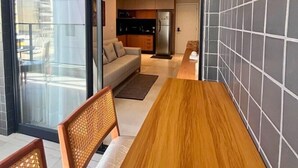 A modern kitchen with a built-in oven, a dining area with a wooden table and chairs, and a view through a glass door. - LM HYDE PARK (João Pessoa)