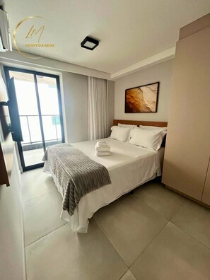 Una habitación de hotel con cama, un cuadro en la pared, una ventana con cortinas y una puerta.