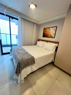 A hotel room with a bed, a large window, a painting on the wall, and a ceiling light. - LM HYDE PARK (João Pessoa)