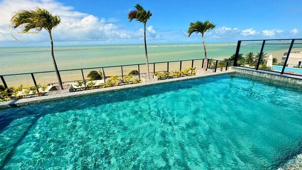 A clear blue pool with a view of the ocean and palm trees. - LM HYDE PARK (João Pessoa)