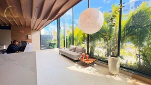 A modern hotel lobby with a large window, a sofa, a coffee table, and a potted plant. - LM HYDE PARK (João Pessoa)