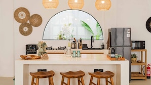 A modern kitchen with a central island, pendant lights, and a large window with a view of greenery. - 2BR Bali Villa Near Uluwatu Surf & Beach Clubs (South Kuta)