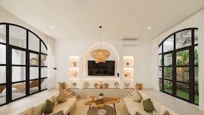 A spacious living room with a large TV, comfortable seating, and a view of greenery through large windows. - 2BR Bali Villa Near Uluwatu Surf & Beach Clubs (South Kuta)