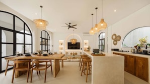 A modern kitchen with a central island, wooden chairs, pendant lights, and a ceiling fan. - 2BR Bali Villa Near Uluwatu Surf & Beach Clubs (South Kuta)