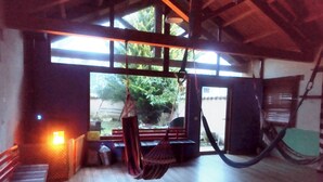 Een kamer met een hangmat, houten vloeren en uitzicht door grote ramen.