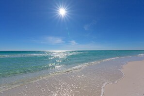 Una spiaggia con acqua cristallina, una riva sabbiosa e un sole splendente nel cielo.