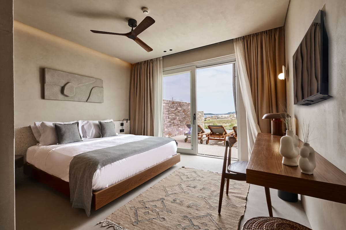 A bedroom with a bed, a ceiling fan, a large window, and a view of the outdoors.