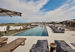 A poolside area with lounge chairs, a pergola, and a view of a coastal town.