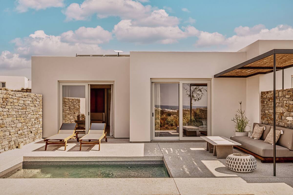A modern outdoor living area with a pool, lounge chairs, and a stone wall.