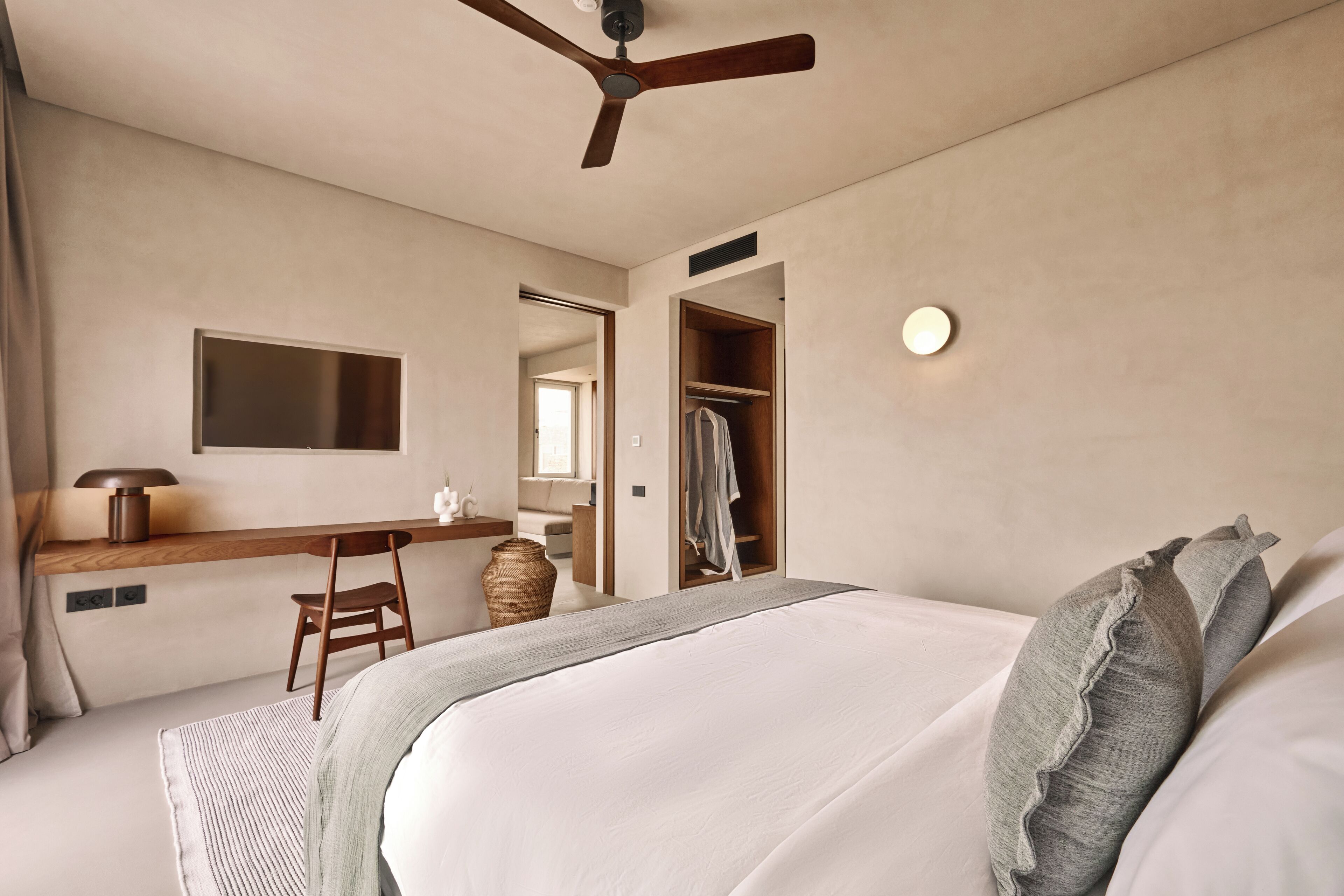 Une chambre à coucher comprenant un lit, un bureau, une chaise, une armoire, un ventilateur de plafond et un miroir.
