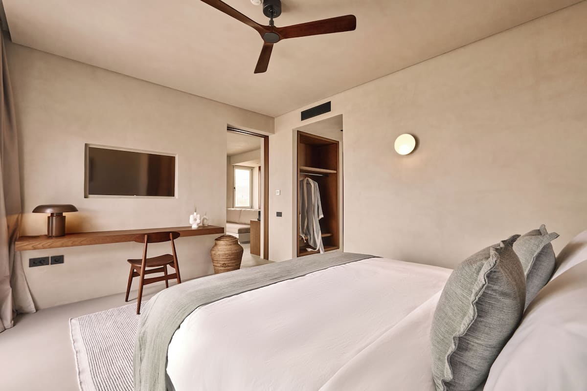 A bedroom with a bed, a desk, a chair, a wardrobe, and a ceiling fan.