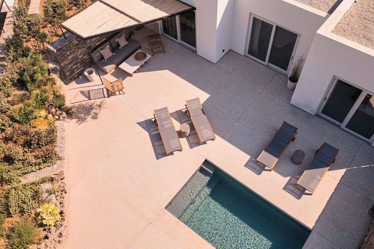 An aerial view of a modern house with a swimming pool, outdoor seating, and a covered patio area.