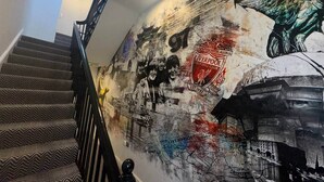 Een trap met een kamerbreed tapijt en een muur met een muurschildering van een voetbalclubembleem en een vogel.