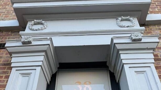 Een gebouwde ingang met het nummer '38' boven de deur, een zwarte deur en een klein raam erboven.