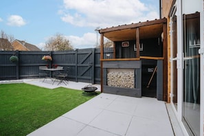 Un patio trasero con terraza, una parrilla, un pozo de fuego y una mesa con sillas.