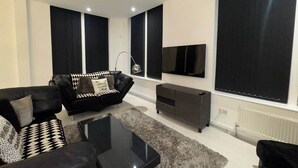 A modern living room with a black sofa, a coffee table, and a TV on the wall.