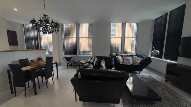 A modern living room with a black sofa, a dining table with chairs, and a chandelier.