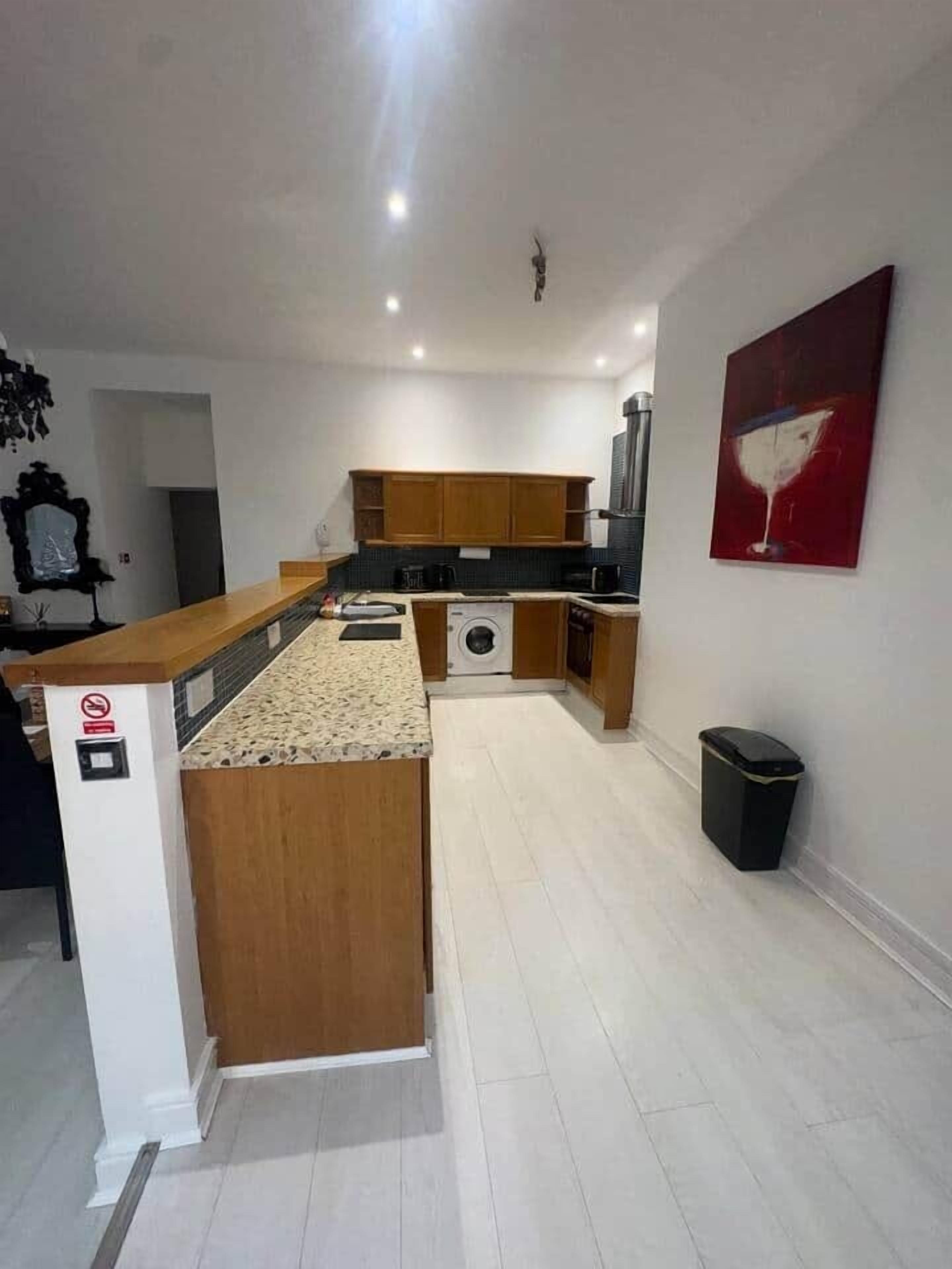 Una cocina moderna con armarios de madera, una isla central, una lavadora y un cubo de basura.
