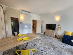 Una sala de estar moderna con una mesa de comedor de madera, sillas amarillas, un televisor de pantalla plana y baldosas de suelo estampadas.
