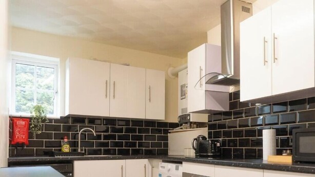 Eine moderne Küche mit weißen Schränken, einer schwarzen Küchenrückwand und Edelstahlgeräten, darunter eine Waschmaschine, ein Backofen und eine Mikrowelle.