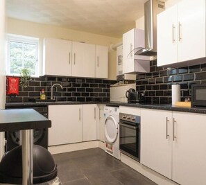 Een moderne keuken met witte kastjes, een zwart betegelde spatwand en roestvrijstalen apparatuur, waaronder een wasmachine, oven en magnetron.