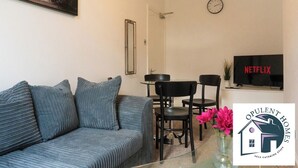 Ein Wohnzimmer mit einer Couch, einem Esstisch mit Stühlen, einem Fernseher und einer Uhr an der Wand.