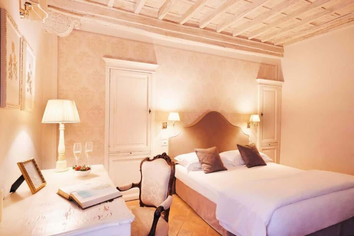 A hotel room with a large bed, two bedside lamps, a chair, a table with a lamp, and a framed picture.