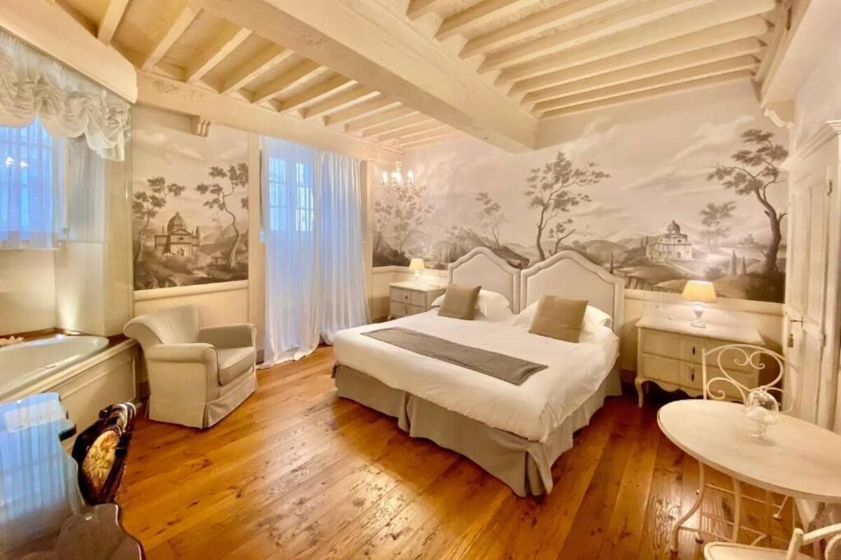 A bedroom with a large bed, a desk, a chair, and a small table.